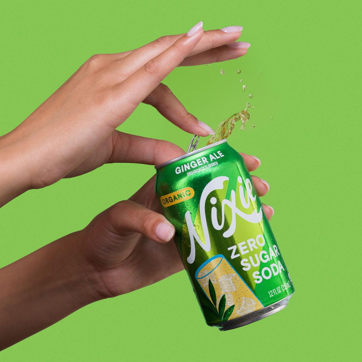 Hands opening a cold can of Nixie Ginger Ale Organic Zero Sugar Soda with liquid splashing from the can against a bright green background.